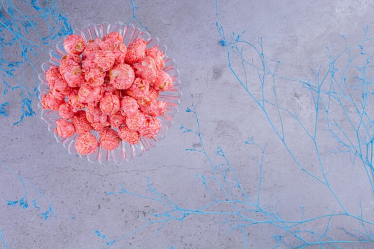 Glass holder with a portion of popcorn candy next to decorative blue branches on marble background